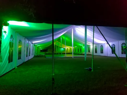 Gran carpa blanca para eventos iluminada de verde por la noche en un campo de hierba.
