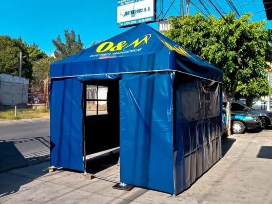 Carpa azul plegable con entrada abierta en una acera junto a una calle, con un coche aparcado y árboles cerca.