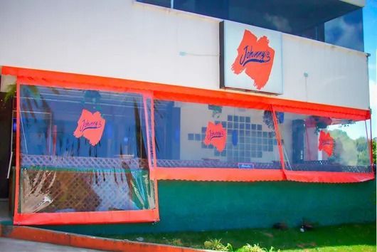 Exterior de un edificio con letreros naranjas y azules y ventanas cubiertas con malla metálica.
