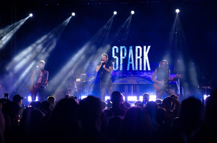 Band performing on a stage outdoors; crowd dancing on grass.