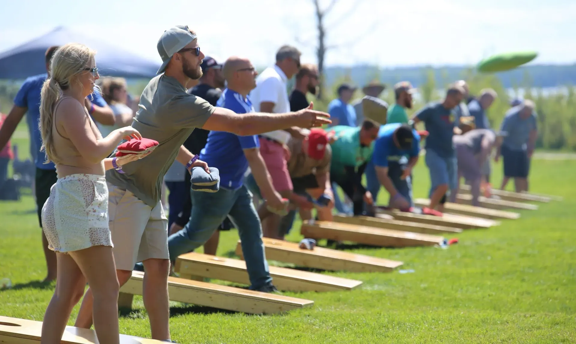 A group of people standing in a line outdoors on grass, participating in a cornhole tournament.