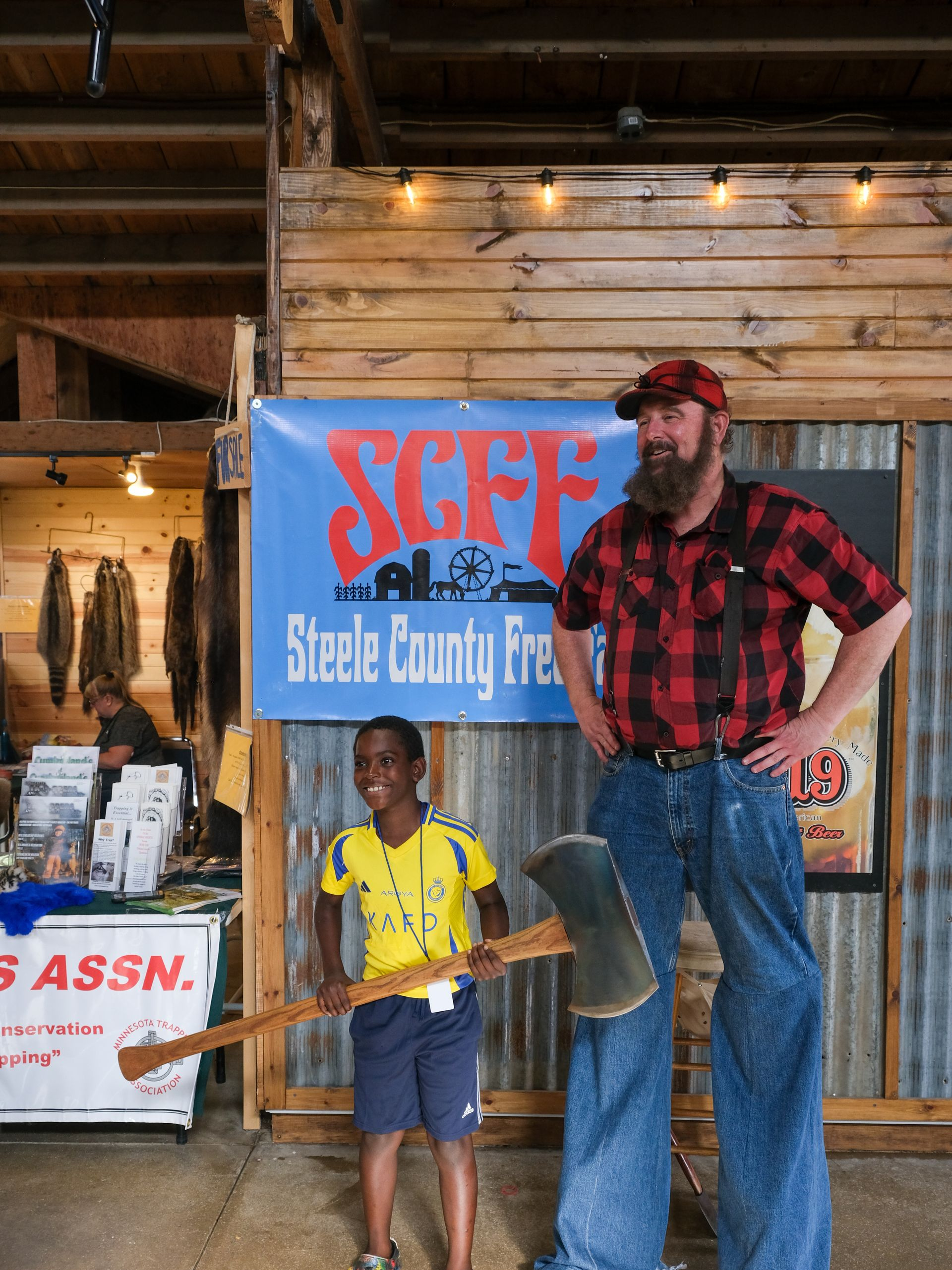Man in red plaid shirt and child hold a shovel before a Steve Cabby Inc. sign in a wooden barn.
