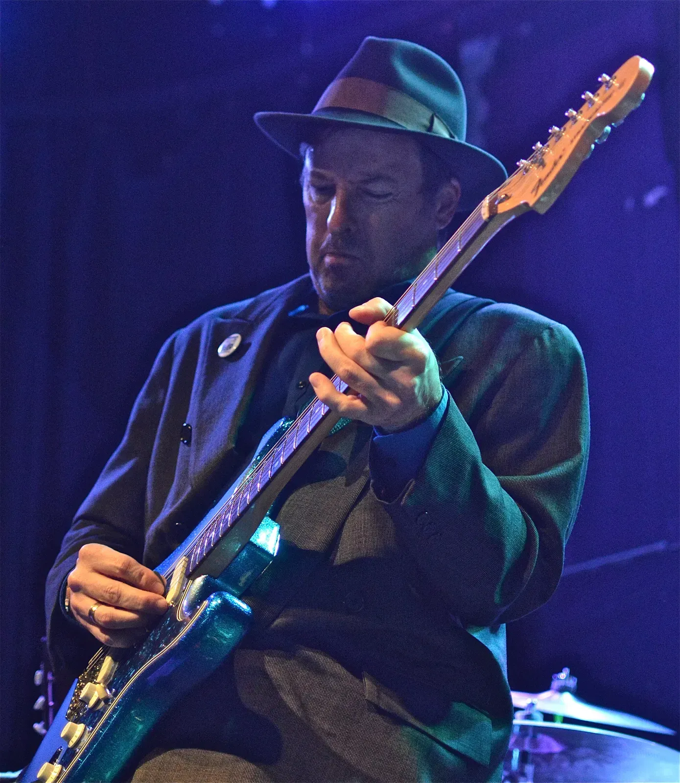 Guitarist in a black hat playing electric guitar on a blue-lit stage
