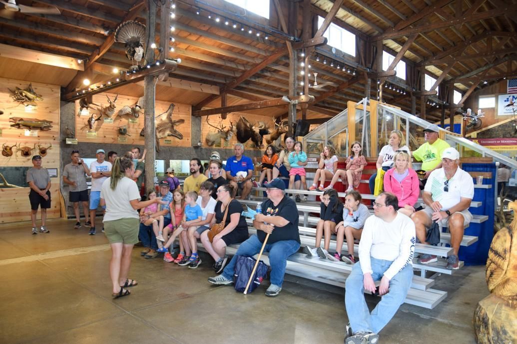 Group seated in a rustic hall watching a presentation, with a speaker at the front and wooden beams overhead