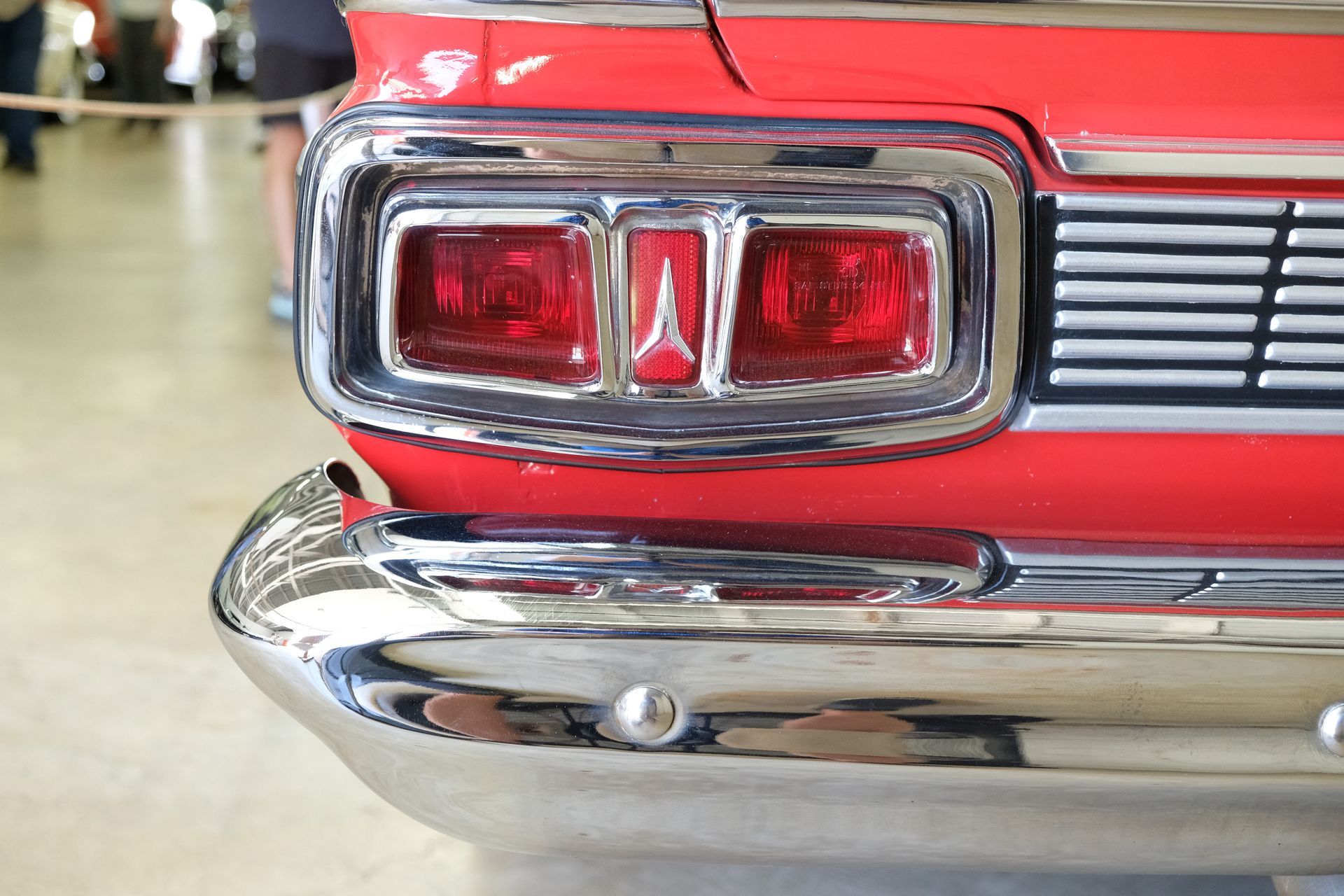 Close-up of a red classic car's tail lights and chrome bumper.