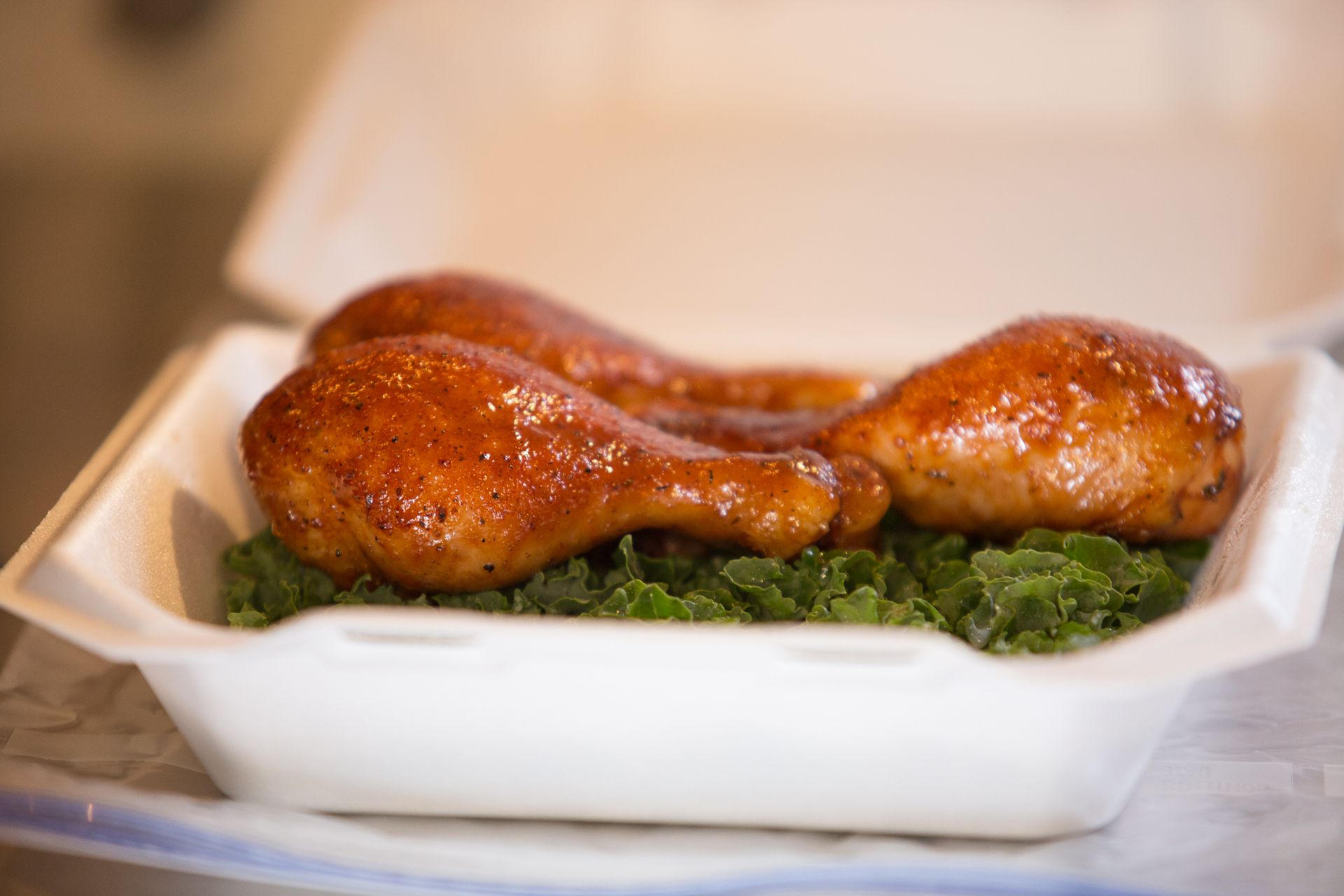 Glazed roasted chicken drumsticks on greens in a white takeout container