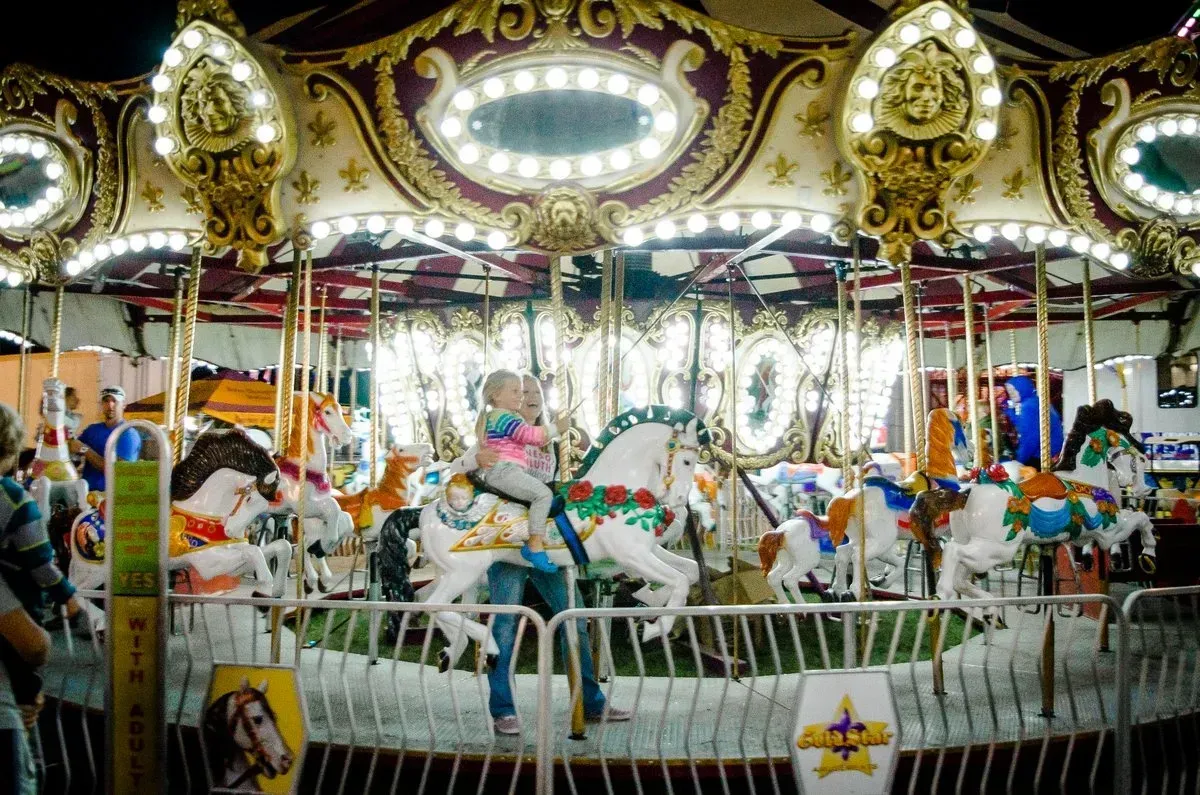 Carousel with brightly lit horses; a child rides a white horse.