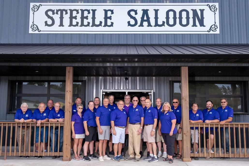 Group of people in blue shirts stand in front of the Steele Saloon.