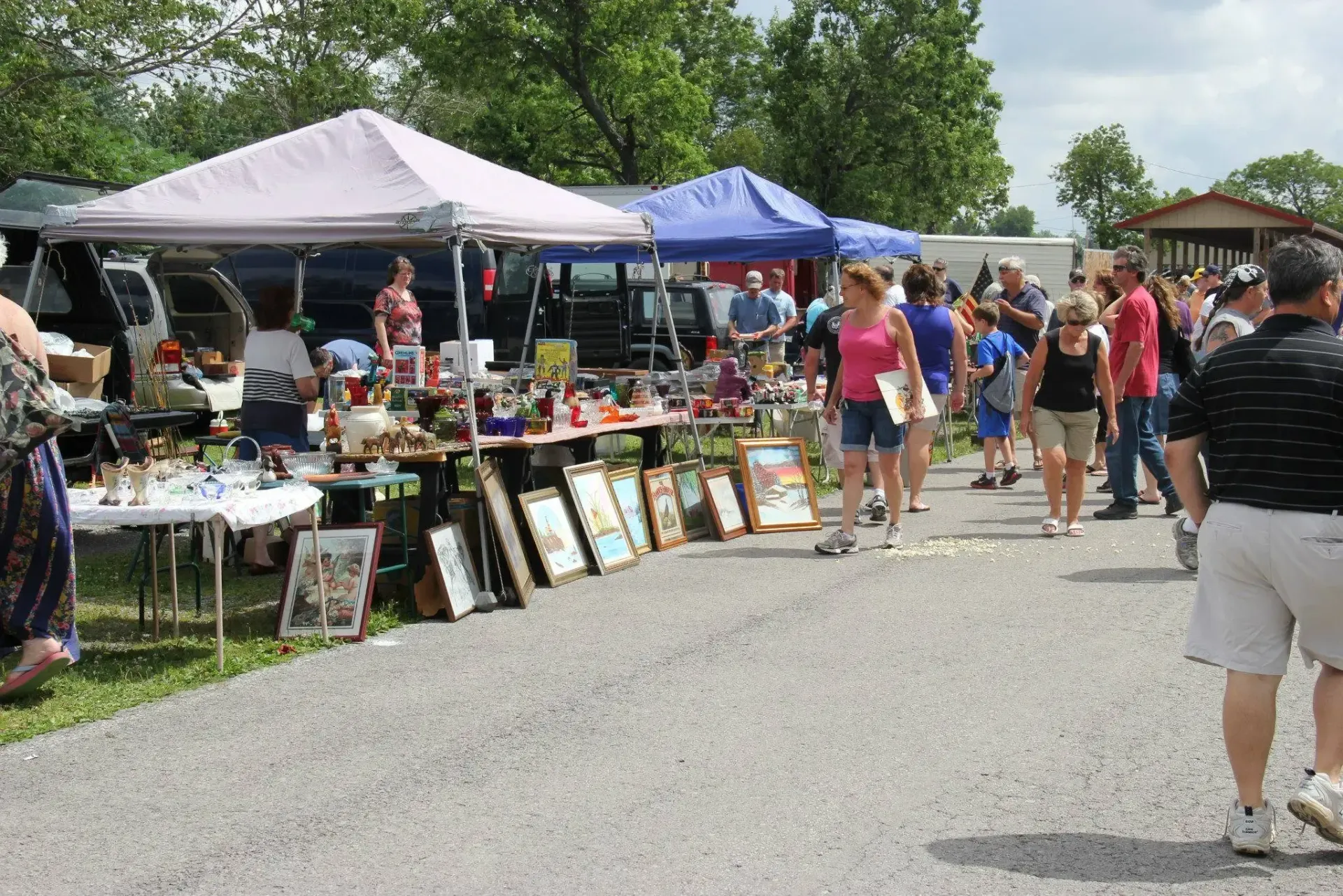 Outdoor flea market with shoppers browsing various items under tents.