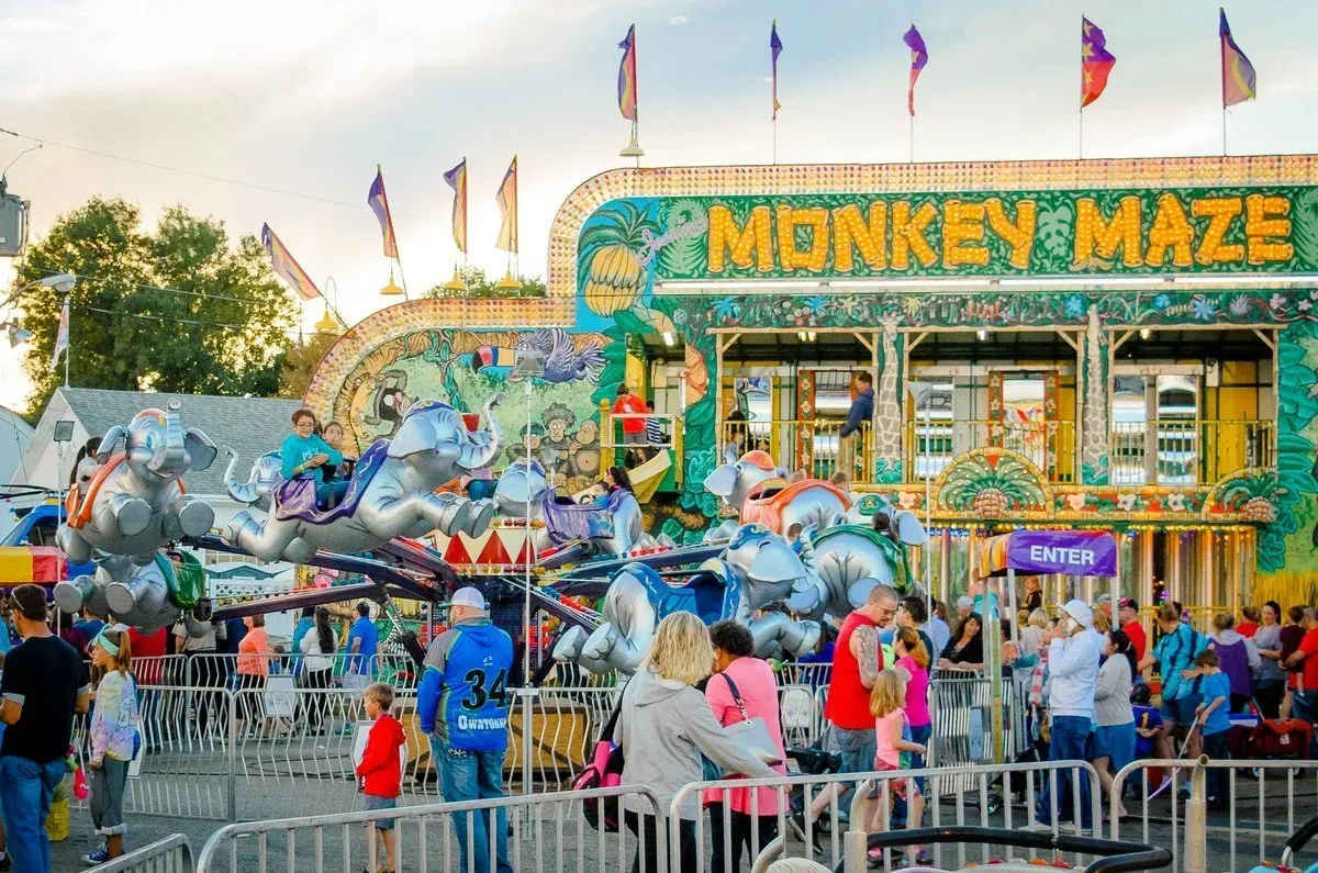 Carnival with Monkey Maze ride, people watching and riding. Bright colors, flags, sunny day.
