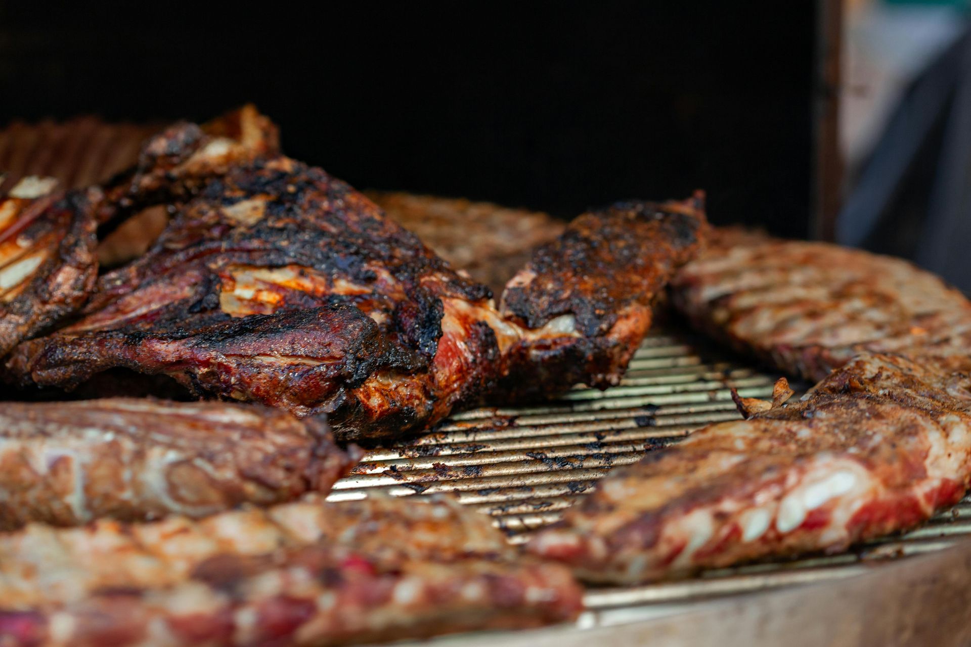 Charred meat sizzling on a grill grate over open flames