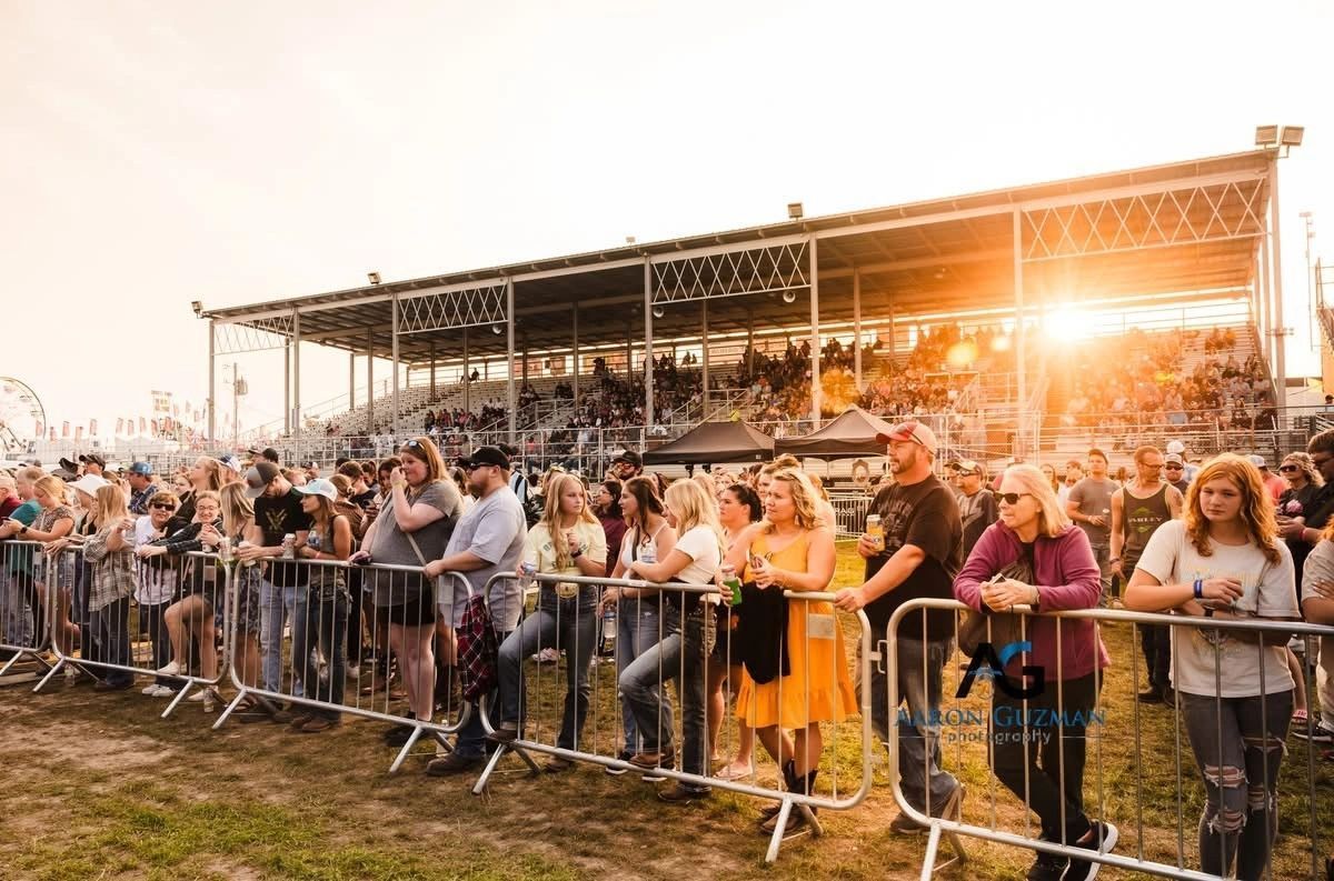 Crowd watches event behind metal barriers, golden sunlight shining on a grandstand.
