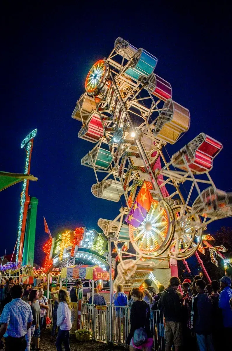 A brightly lit carnival ride at night with colorful seats spinning and a crowd watching.