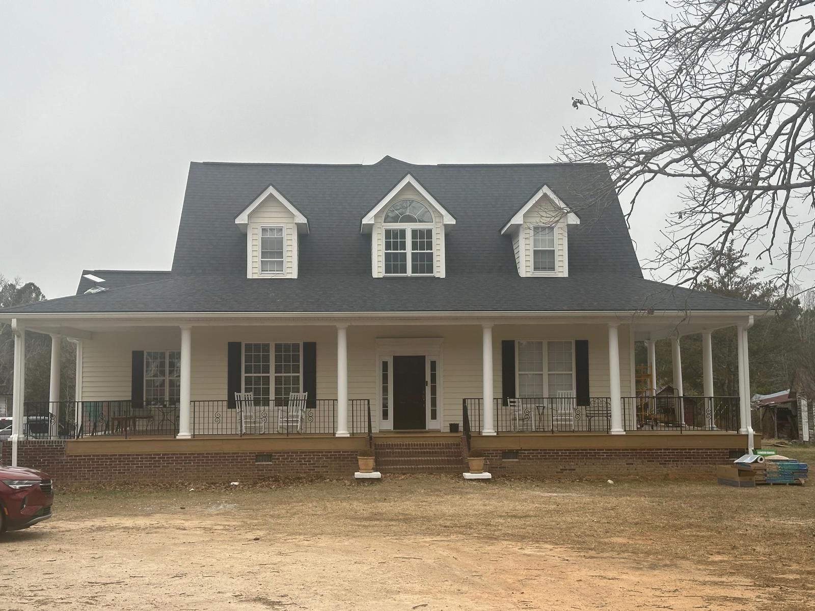White farmhouse with porch, black shutters, and dark roof, under a cloudy sky.