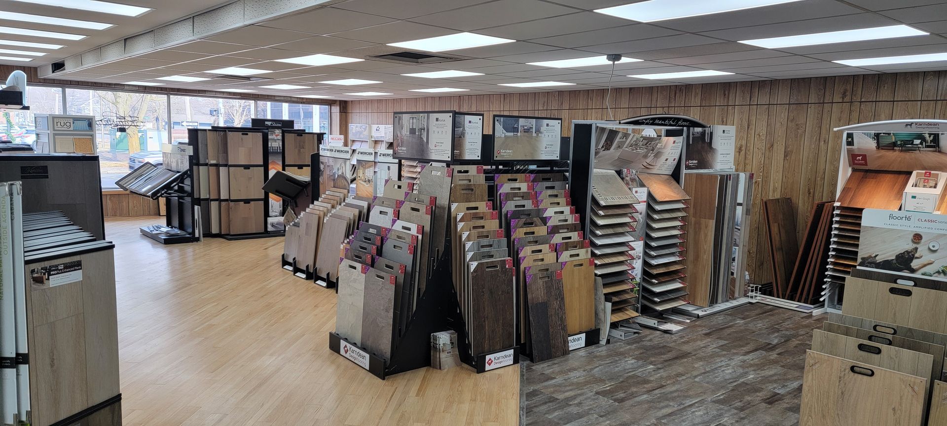 Interior of a flooring store displaying various samples of flooring options. Bright overhead lighting. Retail store interior with racks of flooring samples, display panels, and carpet swatches under bright ceiling lights