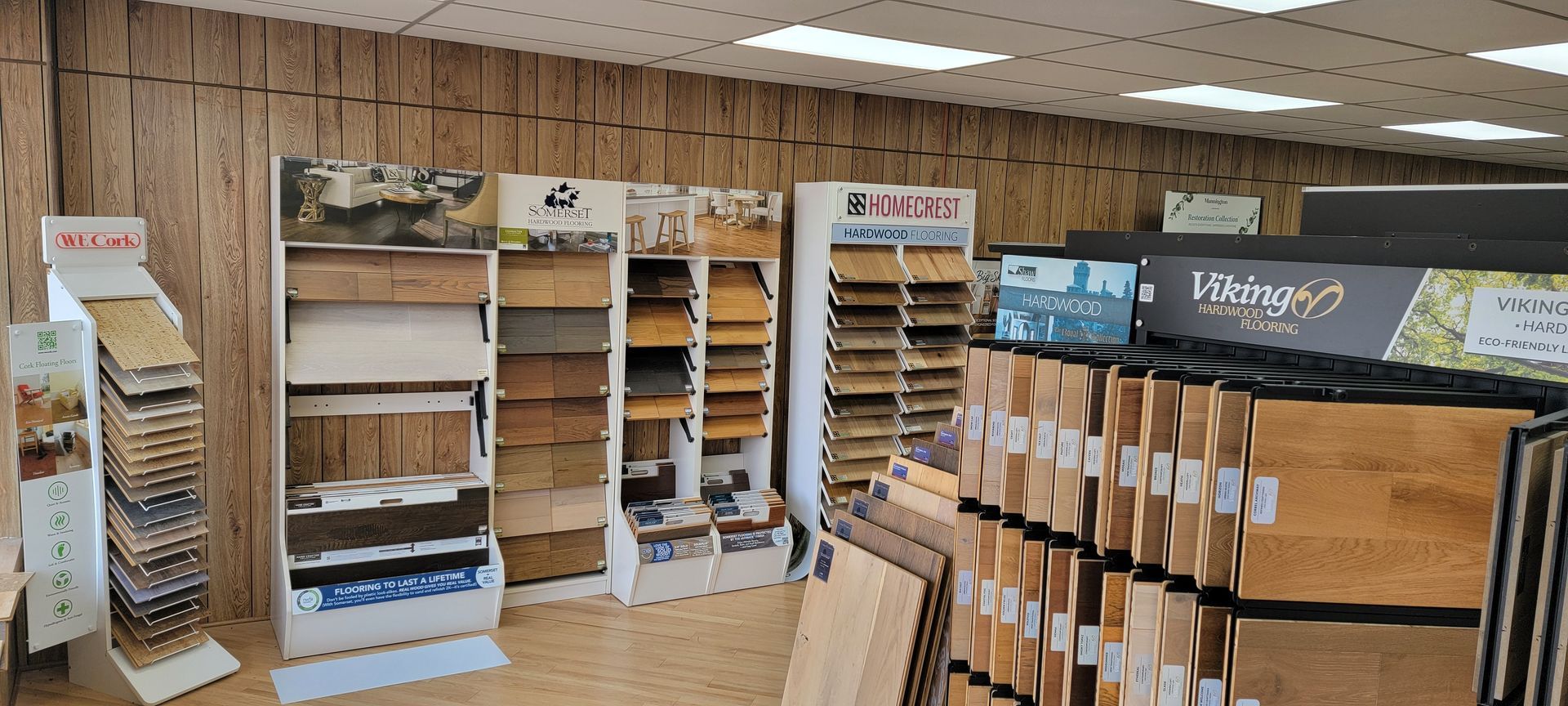 A flooring store interior with displays of wood flooring samples. Wood-paneled retail store aisle with shelves of small wooden items and display racks under bright lights