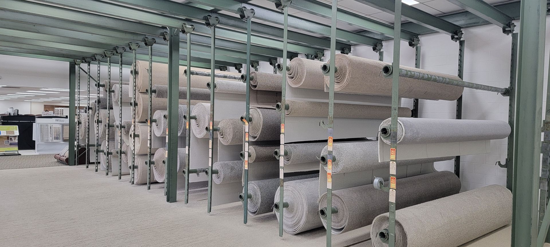 Industrial warehouse shelves stacked with large rolls of fabric or carpet in a storage aisle