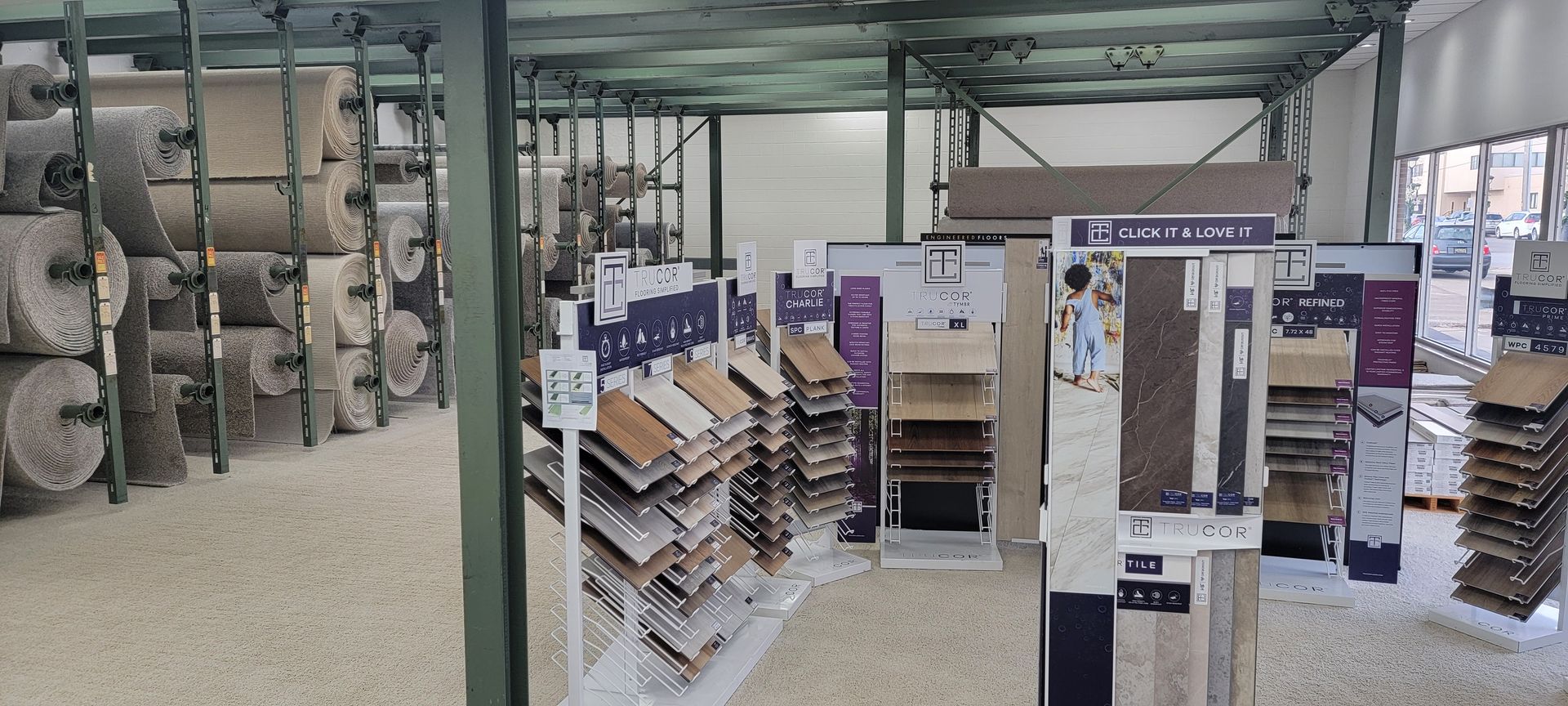 Interior of a flooring store with rolls of carpet on racks and displays of flooring samples. Indoor warehouse aisle with shelves of boxes and stacked goods under a metal roof