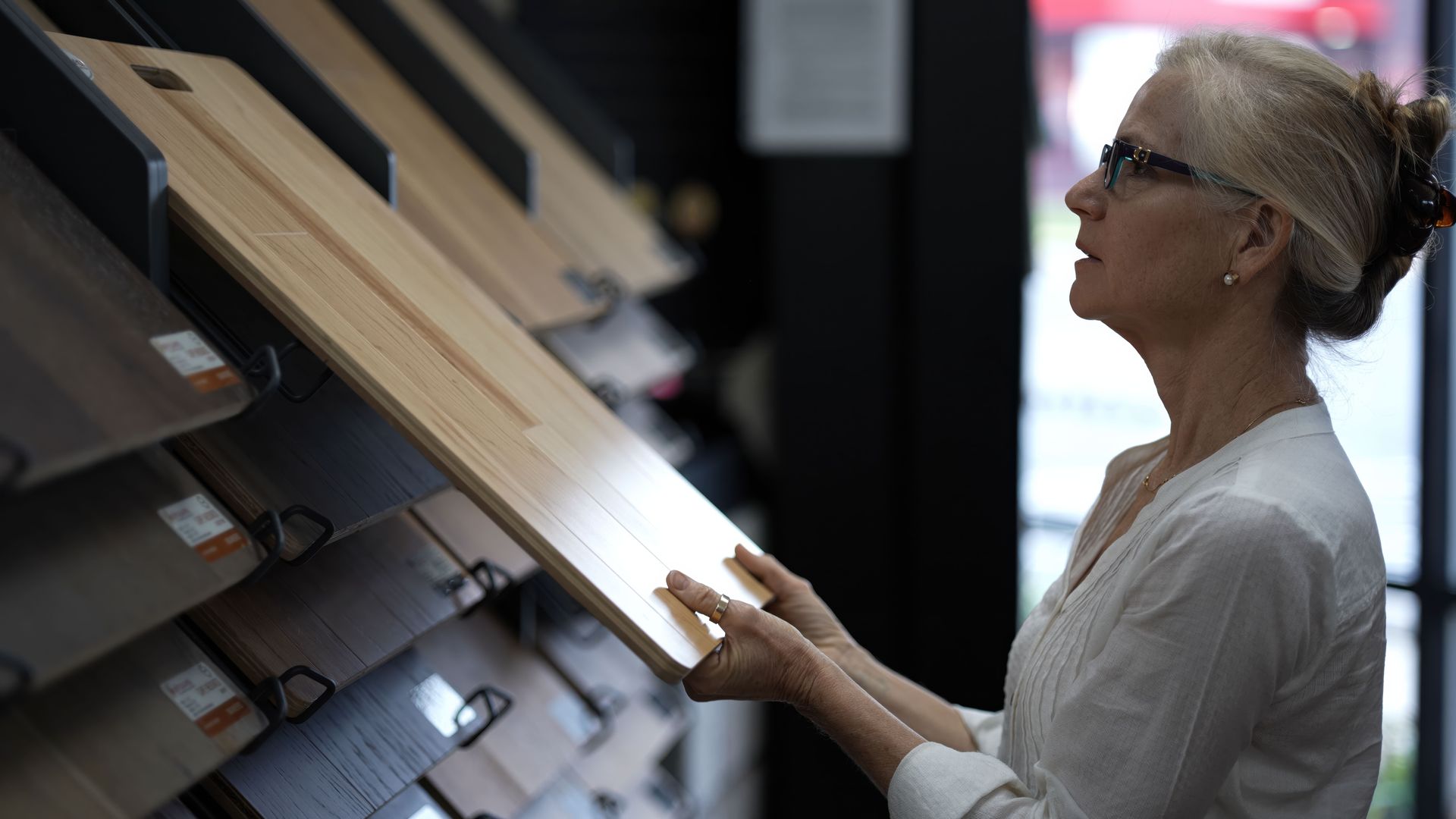Wood veneer samples fanned out on a wood-grain surface, showcasing various shades and patterns. Woman in glasses examining wood samples on display in a showroom