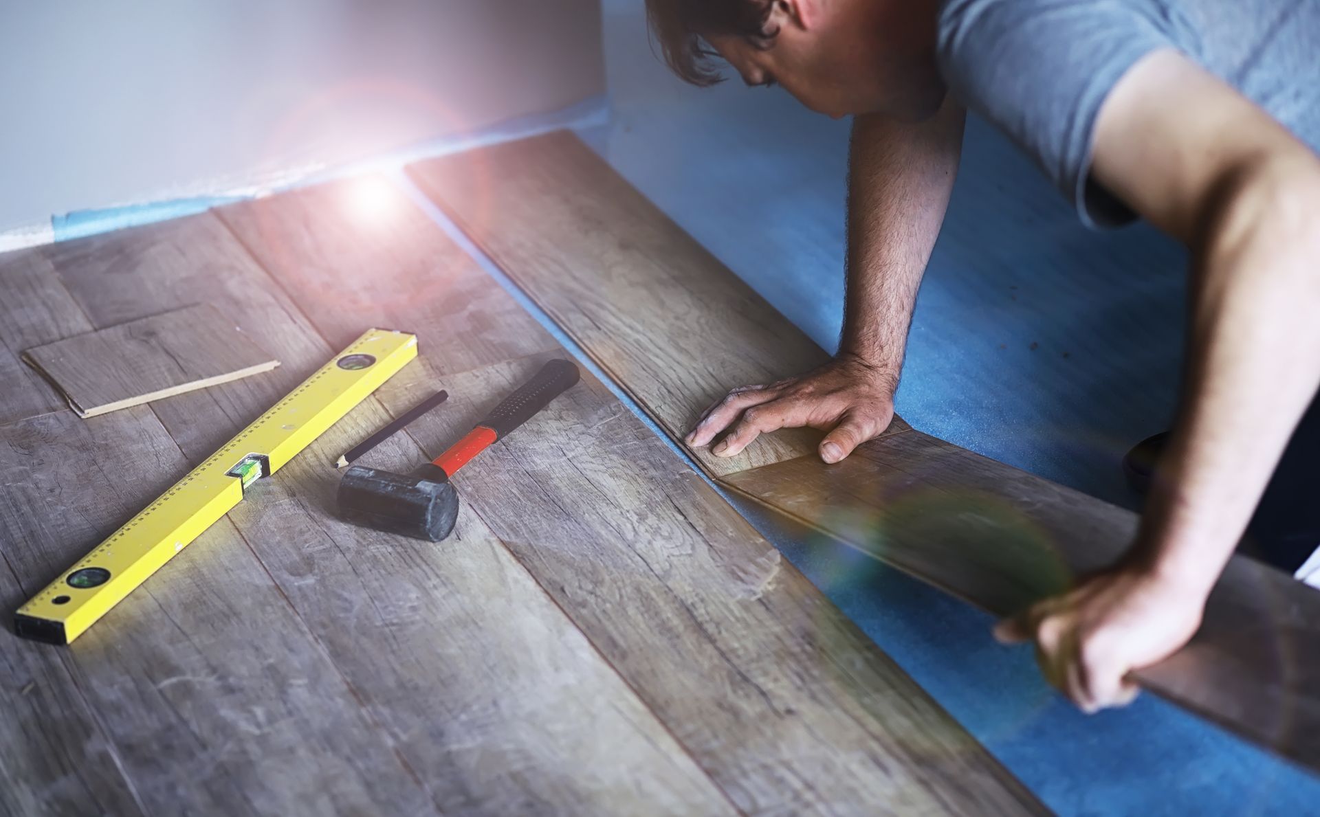 Wooden flooring samples in various light shades, arranged for comparison. Person installing a floor tile with a level and mallet on a wood-patterned floor