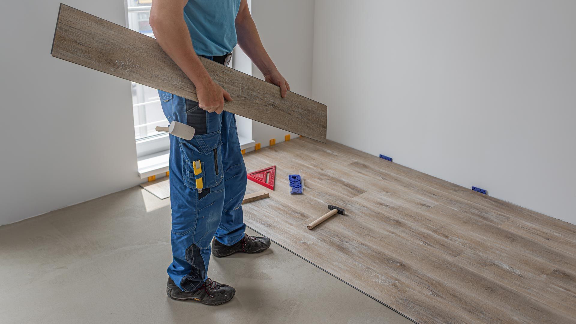 A worker's hands holding a vinyl plank flooring with a click system. Person installing wood flooring in a room, holding planks over a partially laid floor.