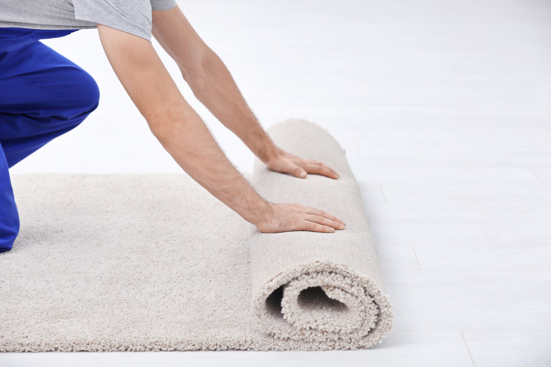Male worker unrolling carpet indoors. Person rolling up a beige carpet on a white floor