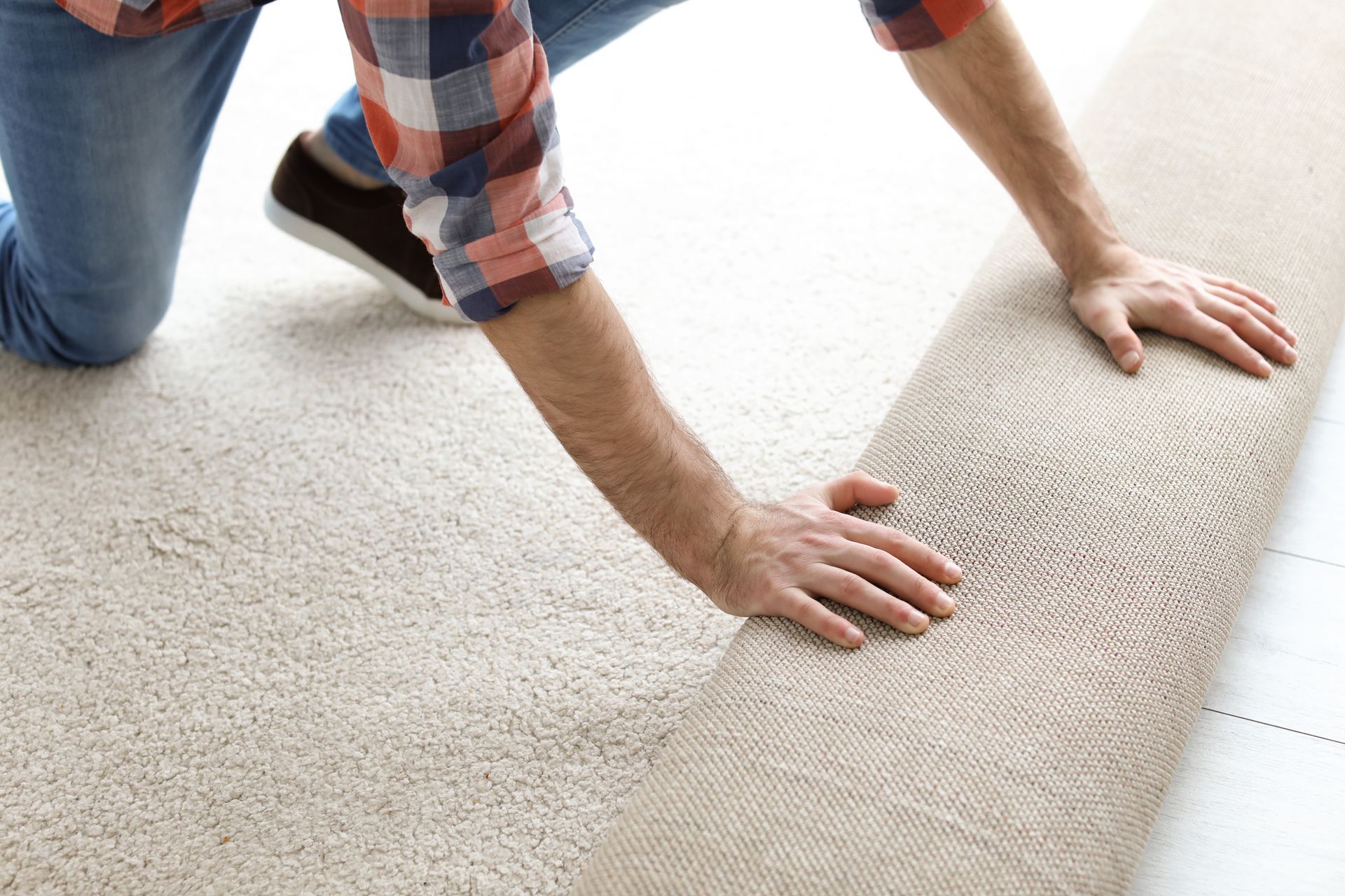 Carpet installation company worker rolling out new carpet flooring in residential living room space. Person rolling up a beige carpet on a white floor