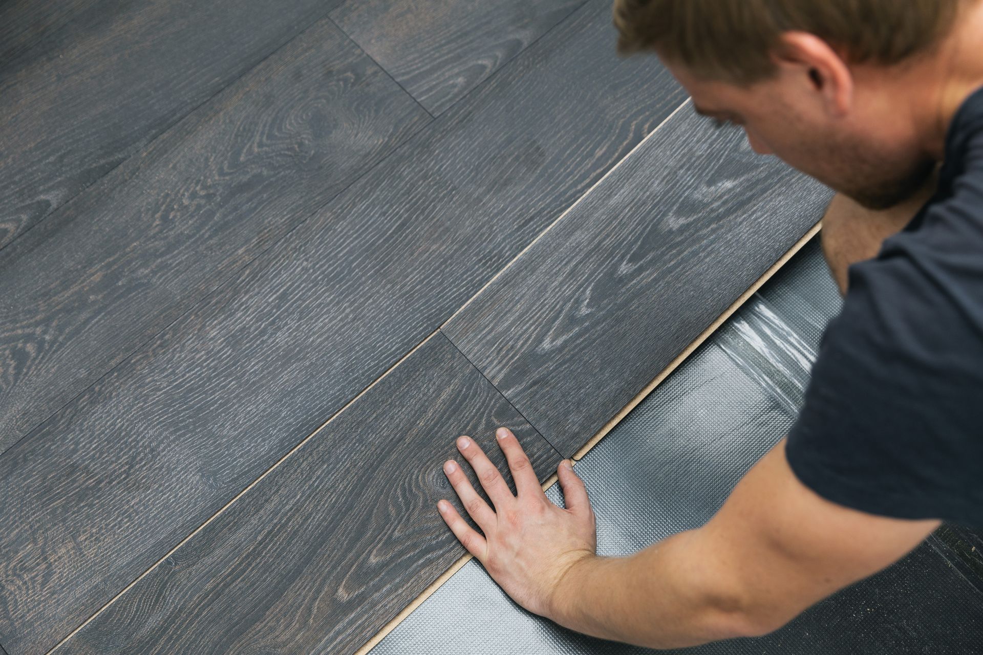 Person installing dark gray laminate flooring. Person installing dark wood flooring with hands on planks