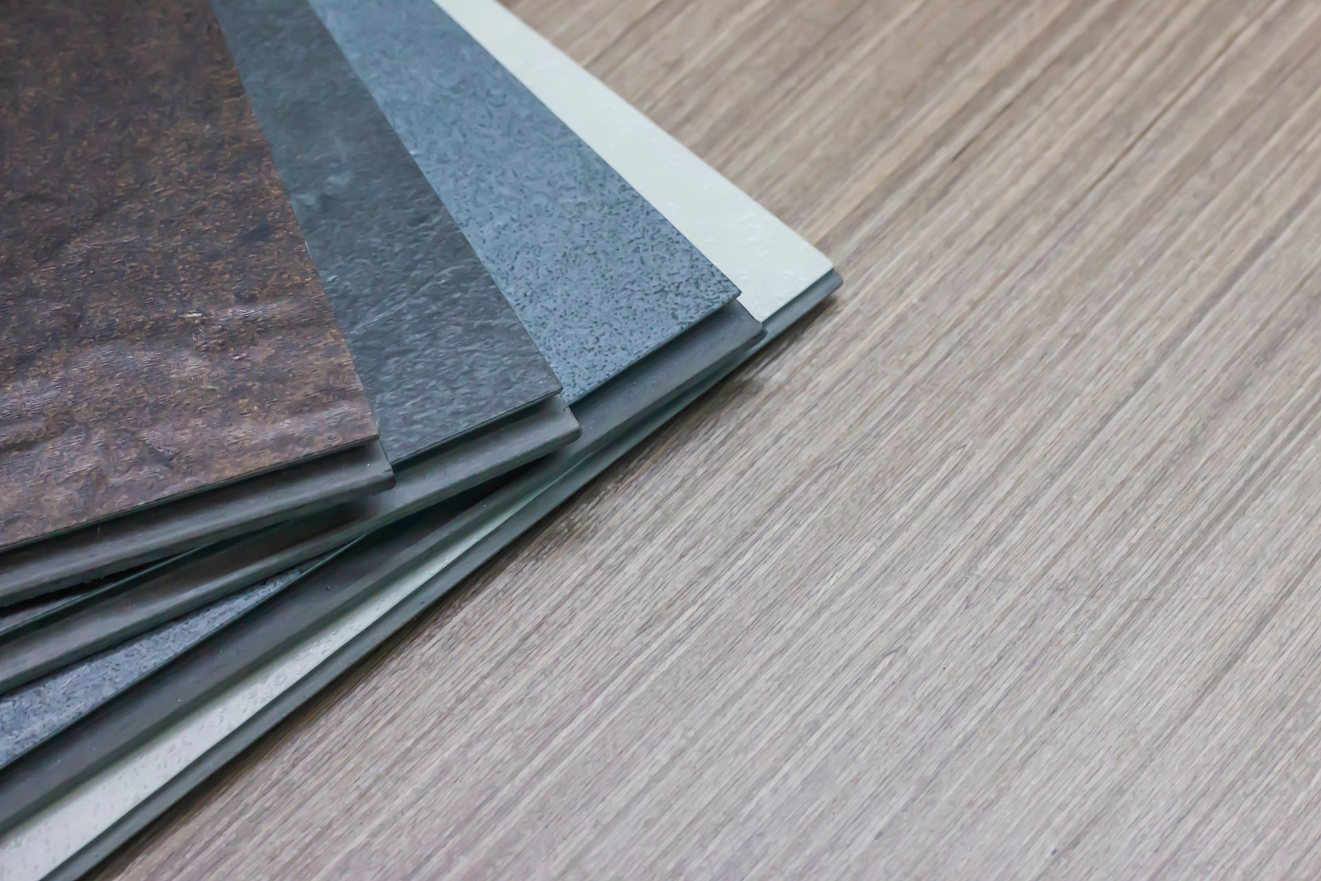Stacked gray and brown flooring samples fanned on a wood-grain surface
