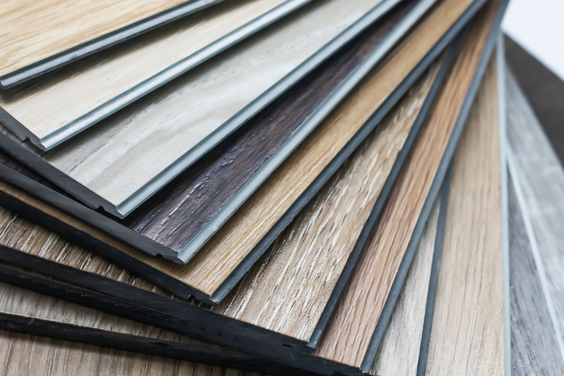Stacked wood-look laminate flooring samples in neutral gray and brown tones
