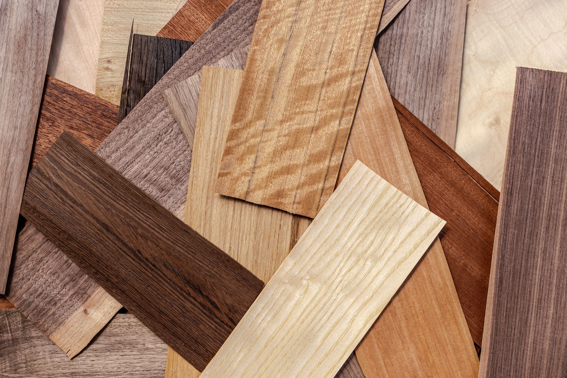 Man holding a fan of wood flooring samples, showing various colors. Assorted wood veneer and laminate samples in brown, tan, and cream tones stacked in a crisscross pattern