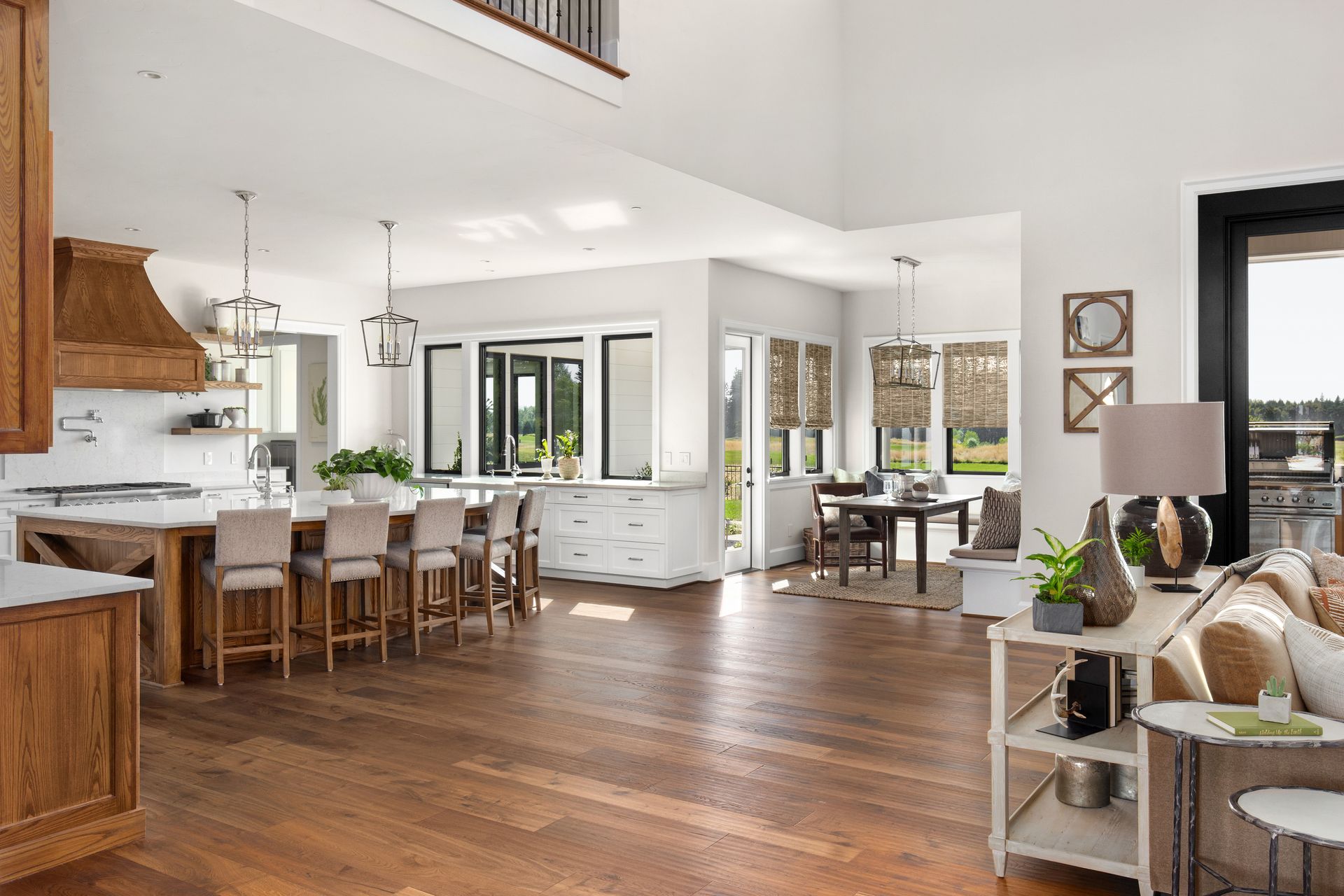 Open-concept kitchen and living area with hardwood floors, a large island, and natural light. Bright open-plan kitchen and living room with hardwood floors, white cabinetry, and a dining table by large windows