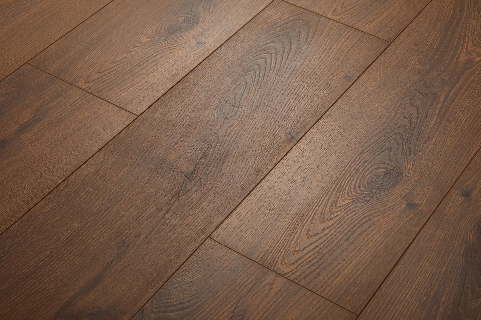 Person installing wood-look vinyl flooring, kneeling. They are bending the flooring over the floor with a troweled adhesive. Close-up of brown wooden floorboards with visible grain and seams