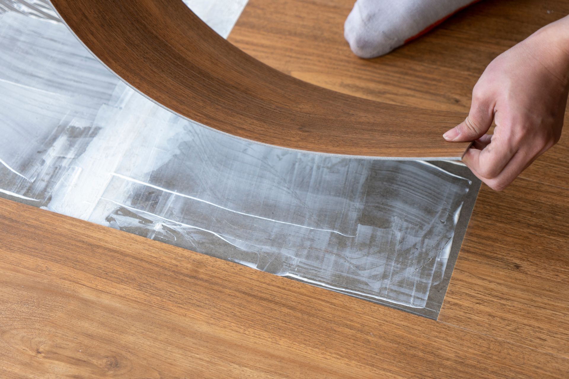 Hands peeling back silver adhesive film from a wood floor surface.