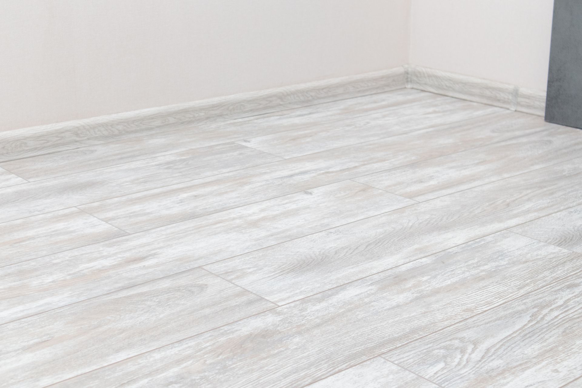 Samples of wood flooring colors, stacked on top of a wood floor. Empty room with light gray wood flooring and white walls.