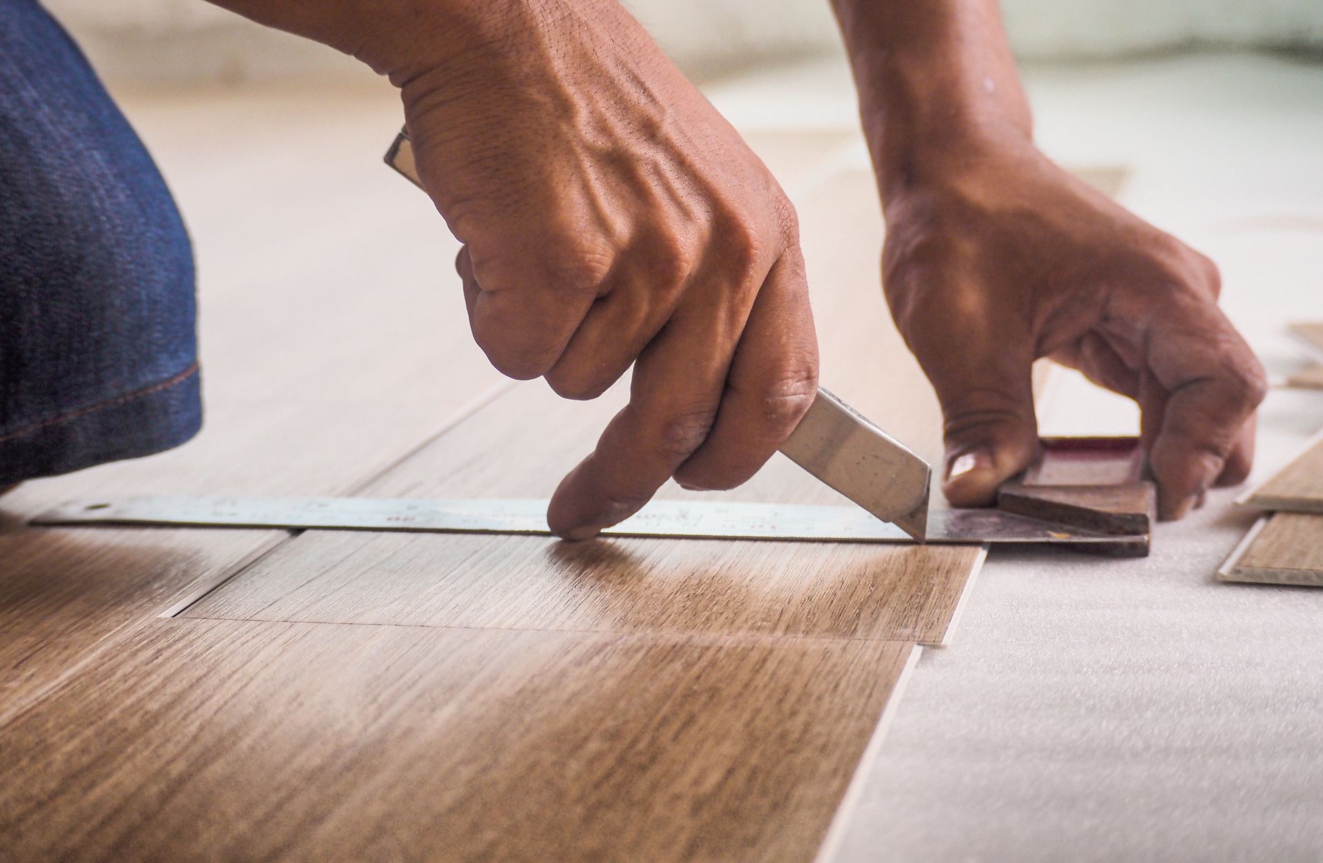 Hands installing wood-look flooring with a tool on a light floor surface.