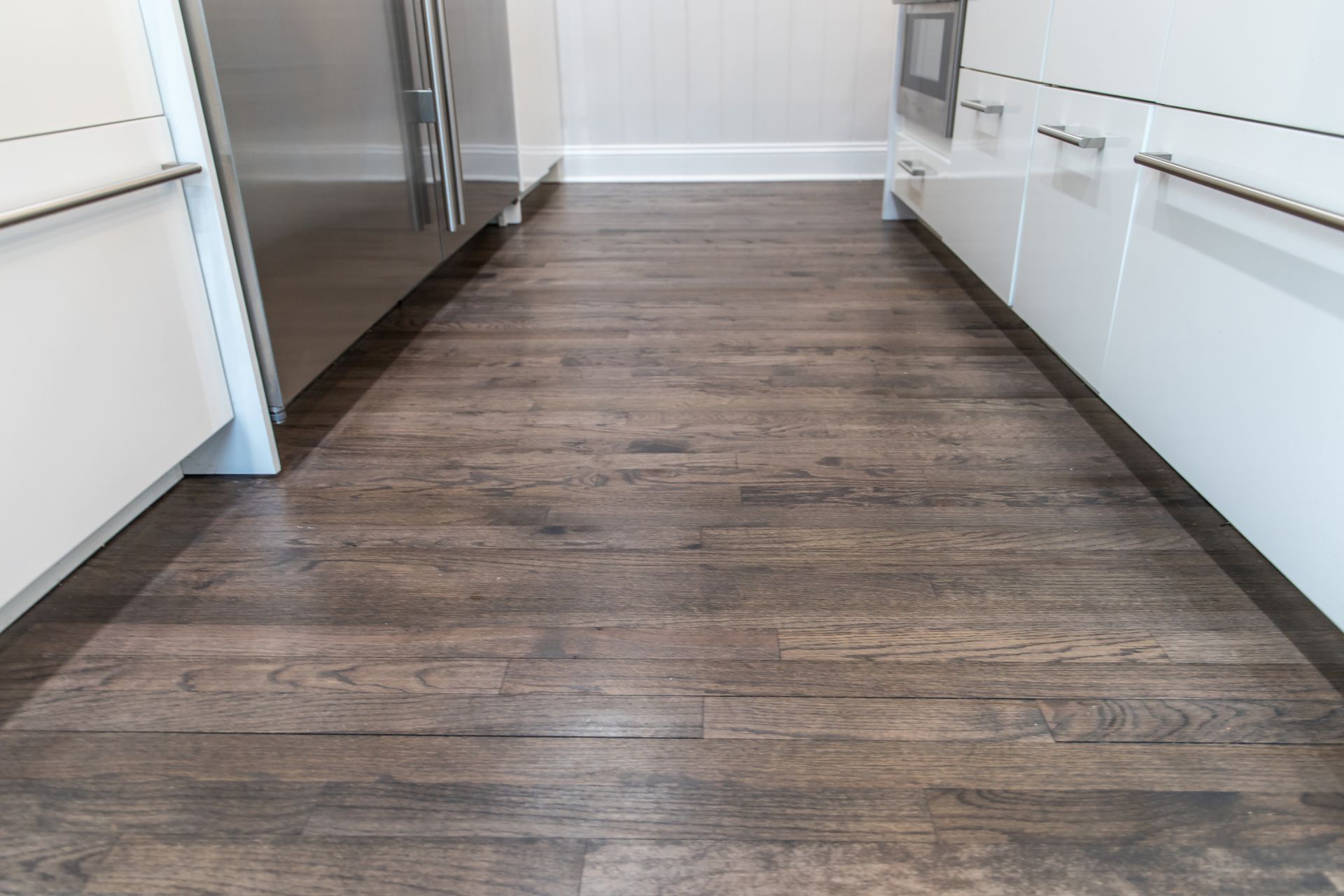 Man holding a fan of wood flooring samples, showing various colors. Modern kitchen with dark wood floor, white cabinets, and stainless steel appliances