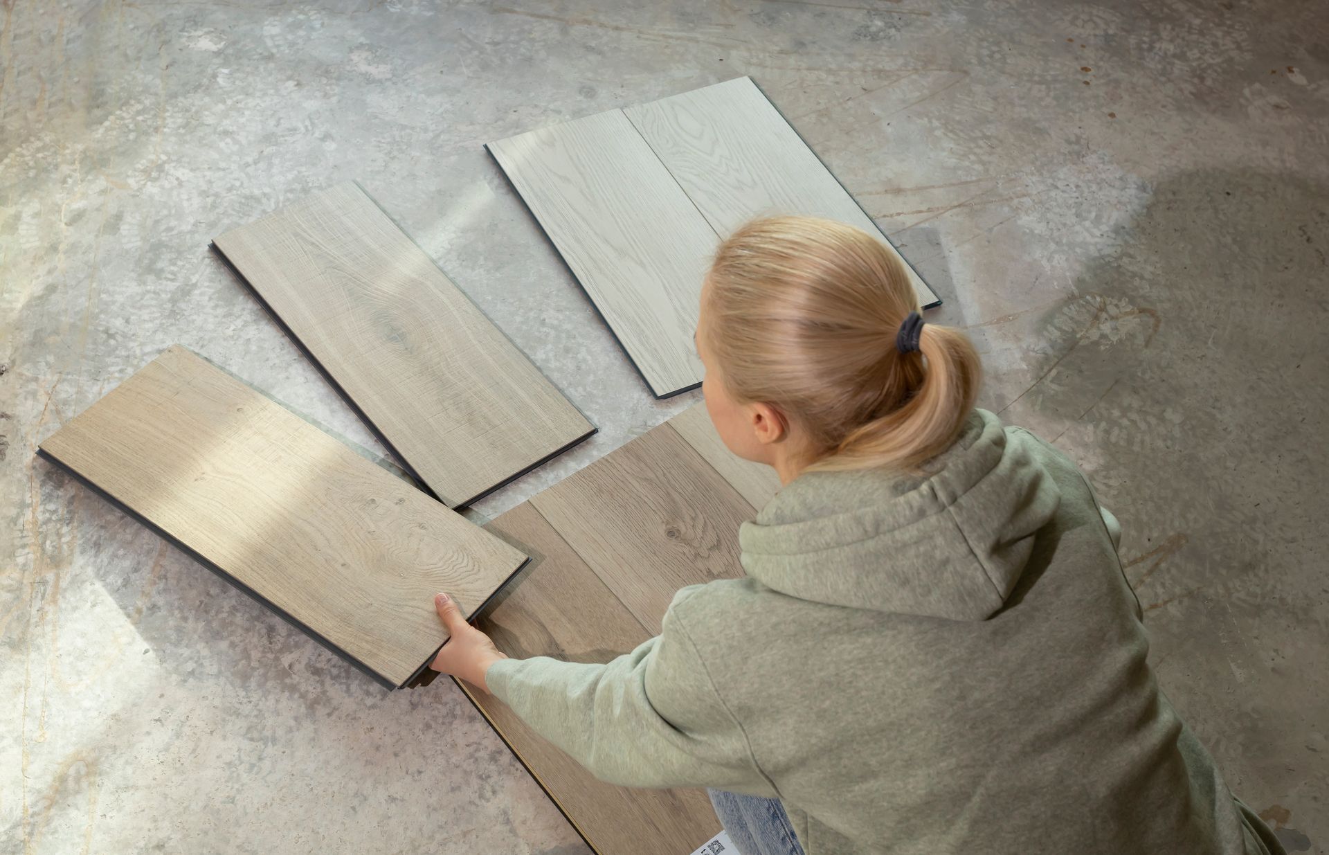 Person installing wood flooring with tools: hammer, level, tape measure. Person placing light wood floor planks on a concrete floor guide