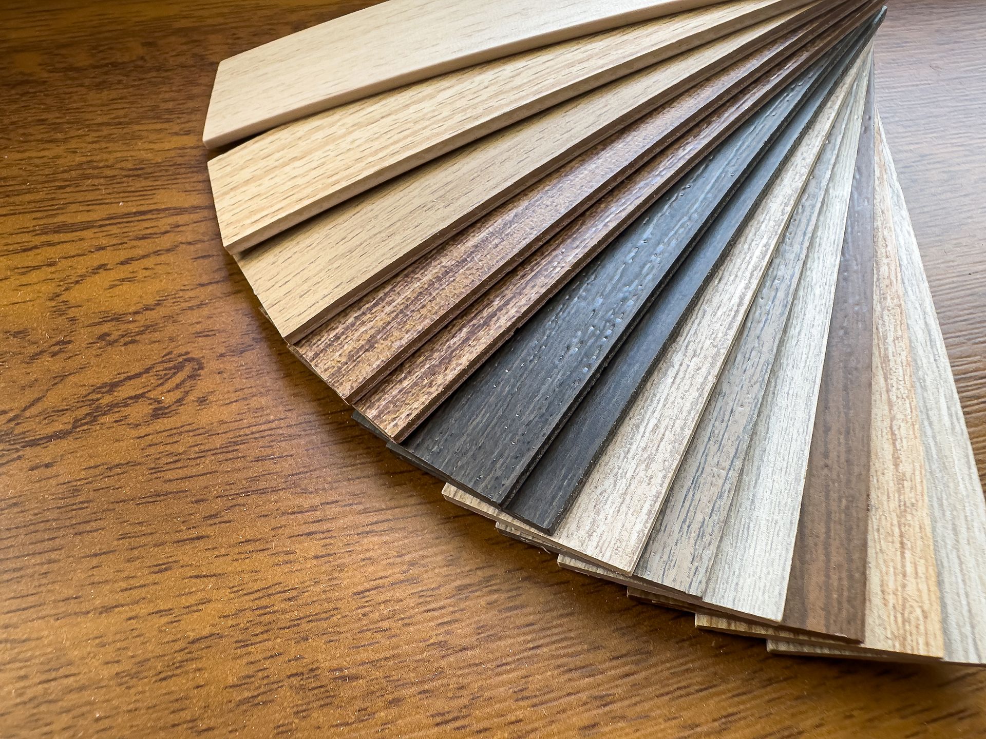 Fan of assorted wood flooring samples on a wooden surface