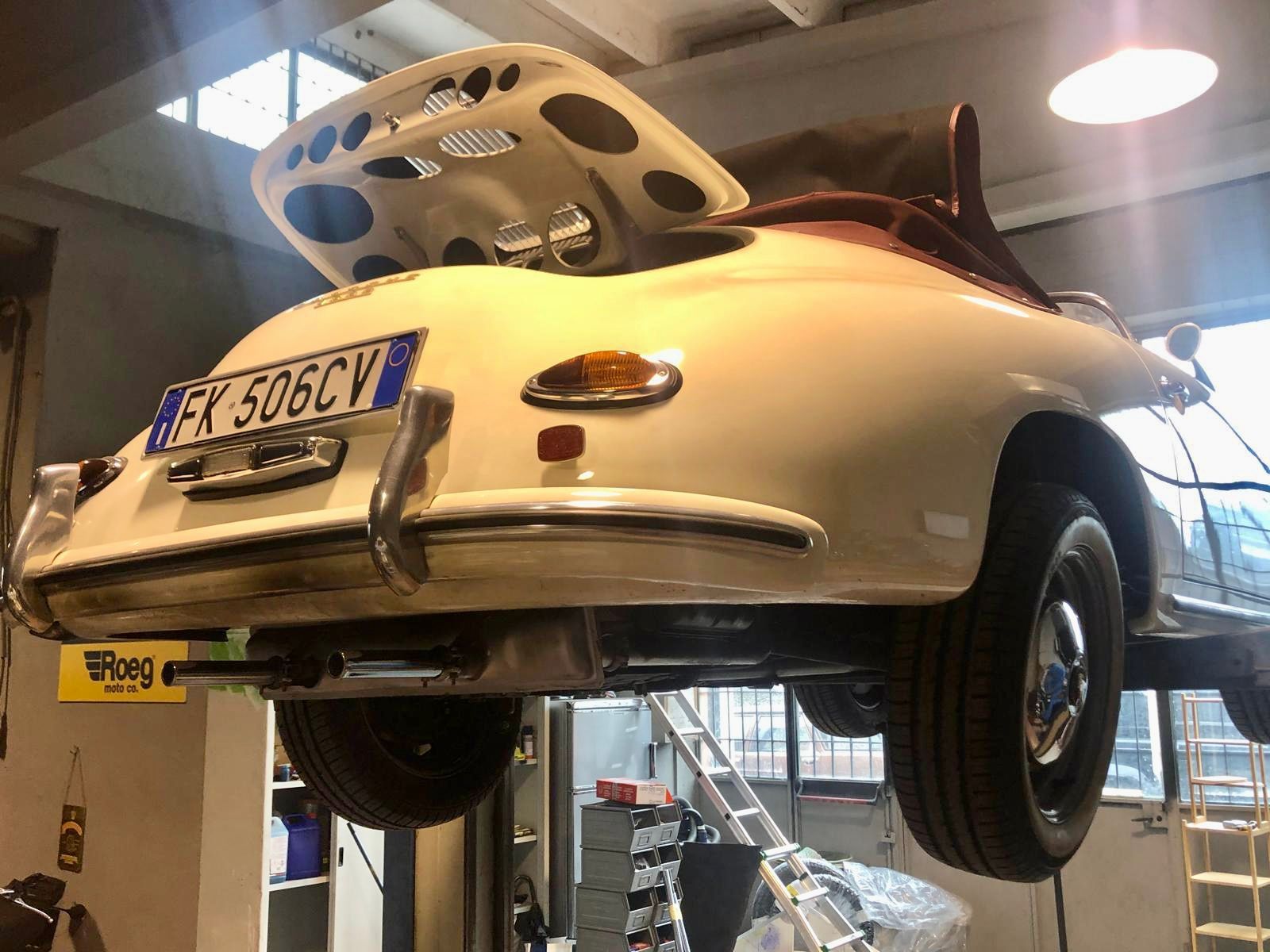 Un'auto bianca con il cofano alzato è su un ponte sollevatore in un garage.