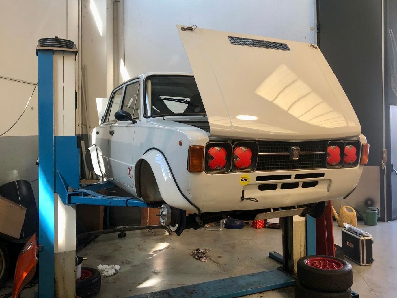 Un'auto bianca è su un ponte sollevatore in un garage con il cofano aperto.