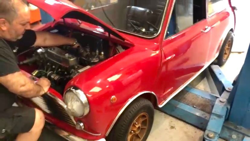 Un uomo sta lavorando su un'auto rossa con il cofano aperto.