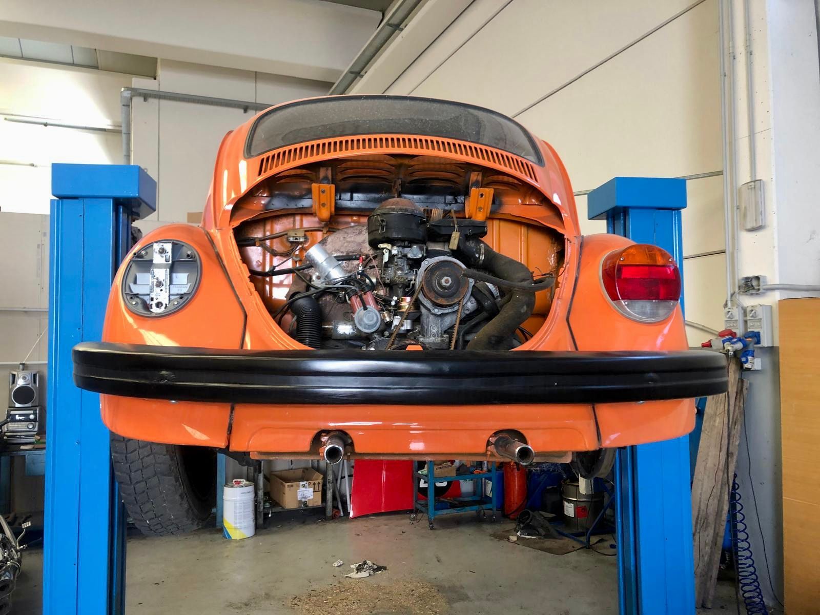 Un maggiolino arancione con il cofano aperto è su un ponte elevatore in un garage.