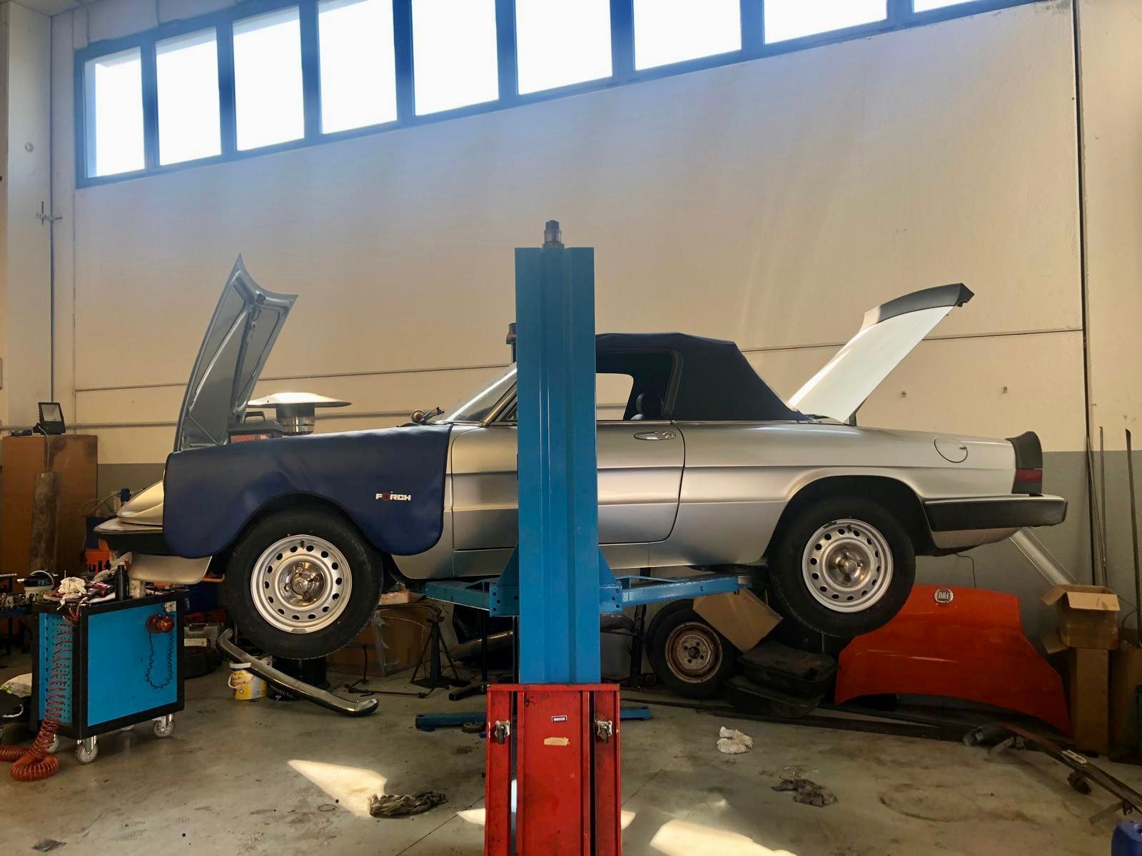 Un'auto è parcheggiata su un ponte sollevatore in un garage con il cofano alzato.