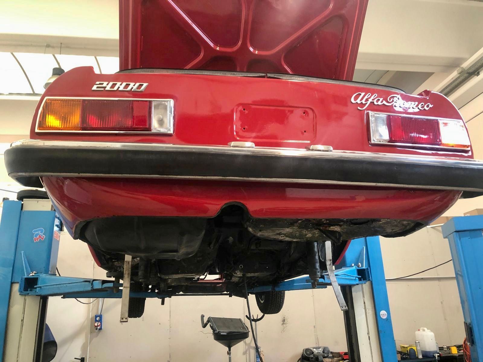 Una alfa romeo 2000 rossa è su un ponte sollevatore in un garage