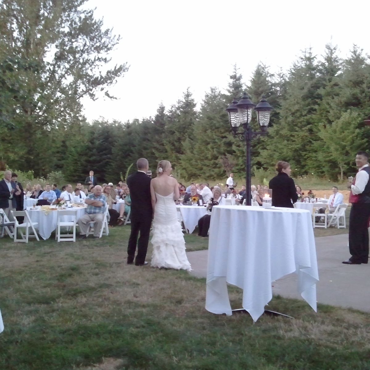 A bride and groom stand in front of a crowd of people at a wedding reception