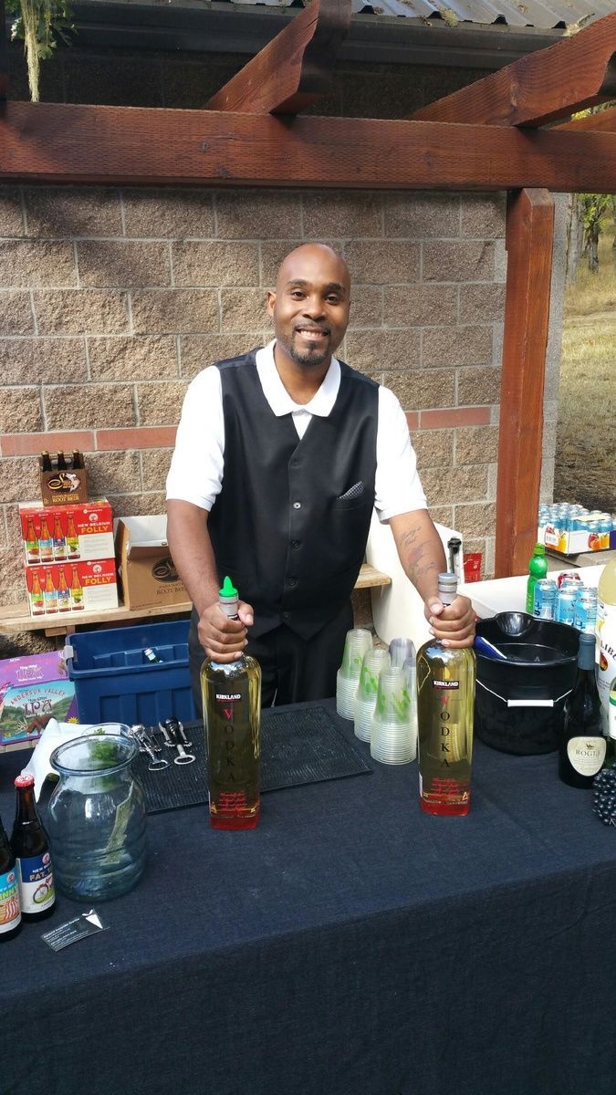A man is standing behind a table with bottles of alcohol on it.