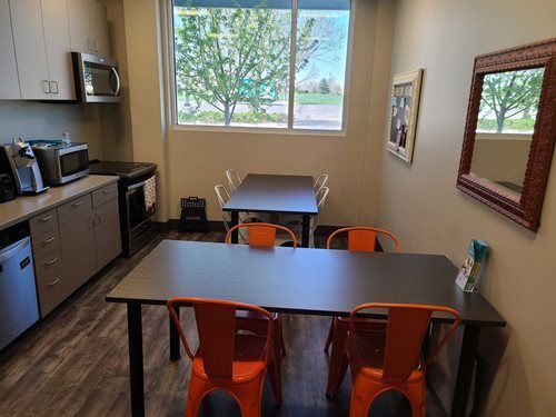 Kitchen area with two tables, orange chairs, cabinets, appliances, and a window.