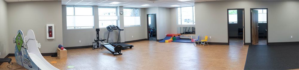 A room with exercise equipment, including a treadmill, and areas for play. Windows and doorways are present.