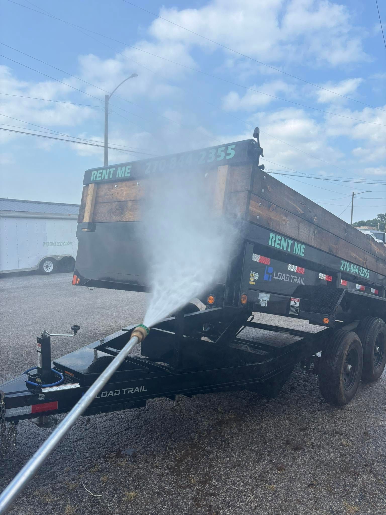 Truck being power washed in a gravel lot, with water spraying from a hose.